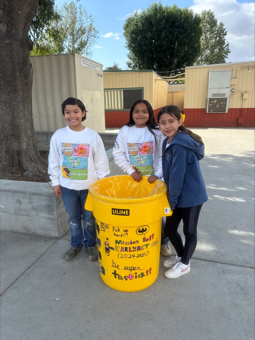 EarlyAct students beside a decorated &ldquo;pick up trash, be super-tastic&rdquo; recycling can on campus
