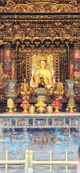 An ornate gilded altar with seated statues and offerings inside Longshan Temple in Taipei