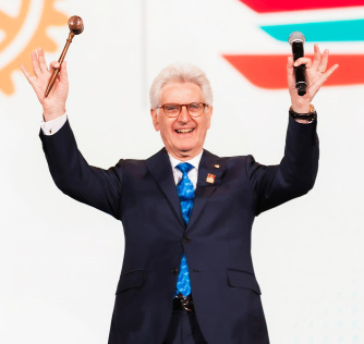 Rotary International President Francesco Arezzo raising a gavel and a microphone with both arms lifted